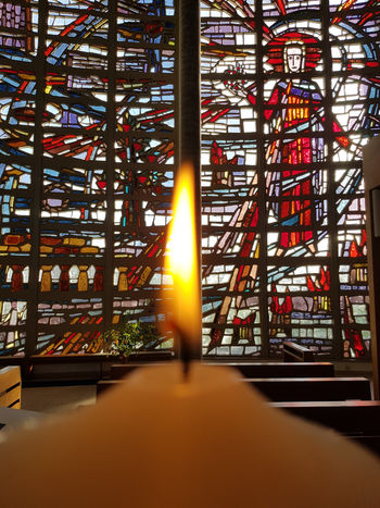 Die Flamme der Osterkerze vor einem Kirchenfenster der Christkönigkirche in Borken. Das Fenster zeigt ein Bild des Auferstandenen. Von ihm geht neues Leben aus.